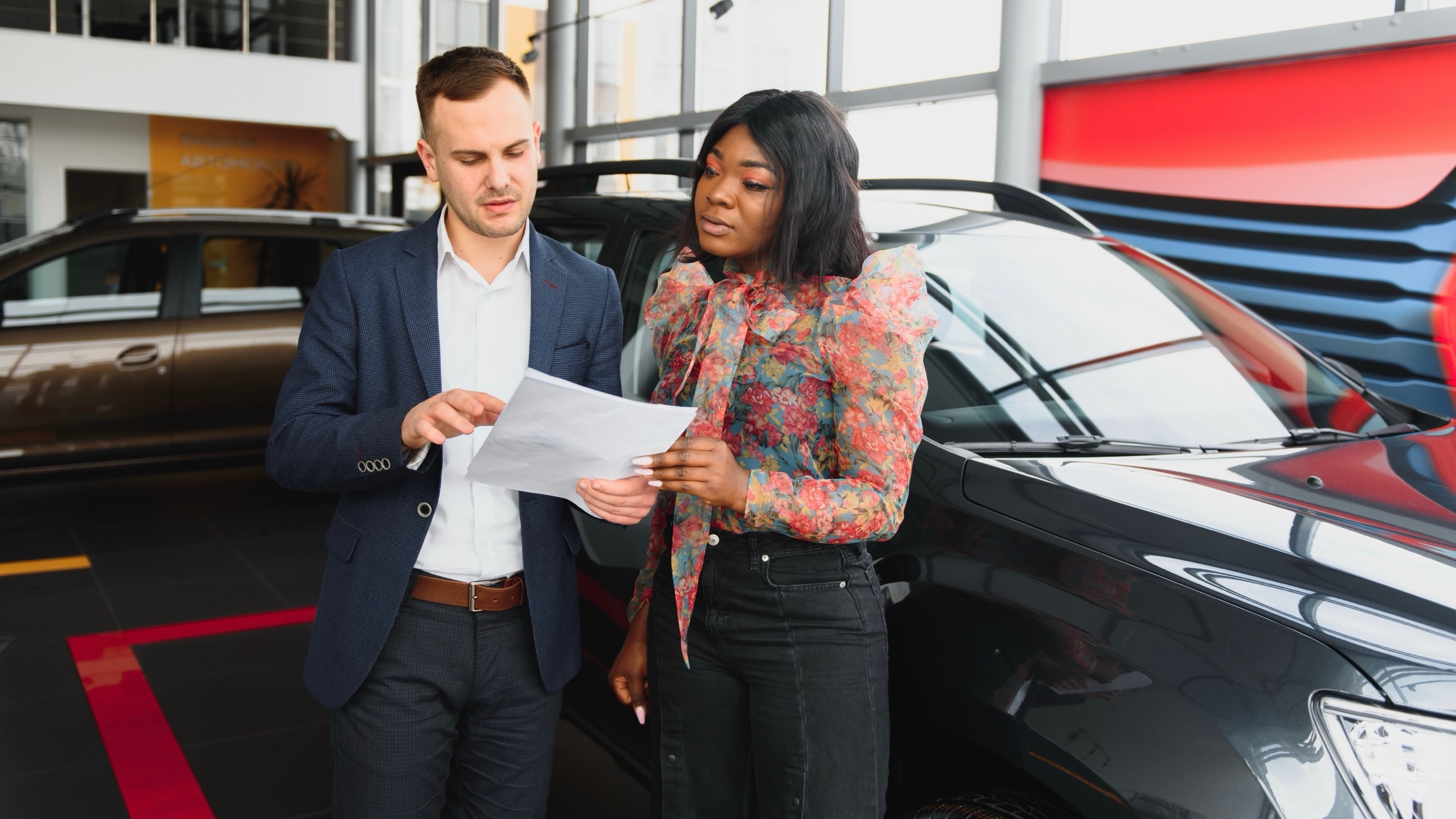 Une vendeuse et un acheteur qui vérifie des papiers pour la vente d'une voiture.