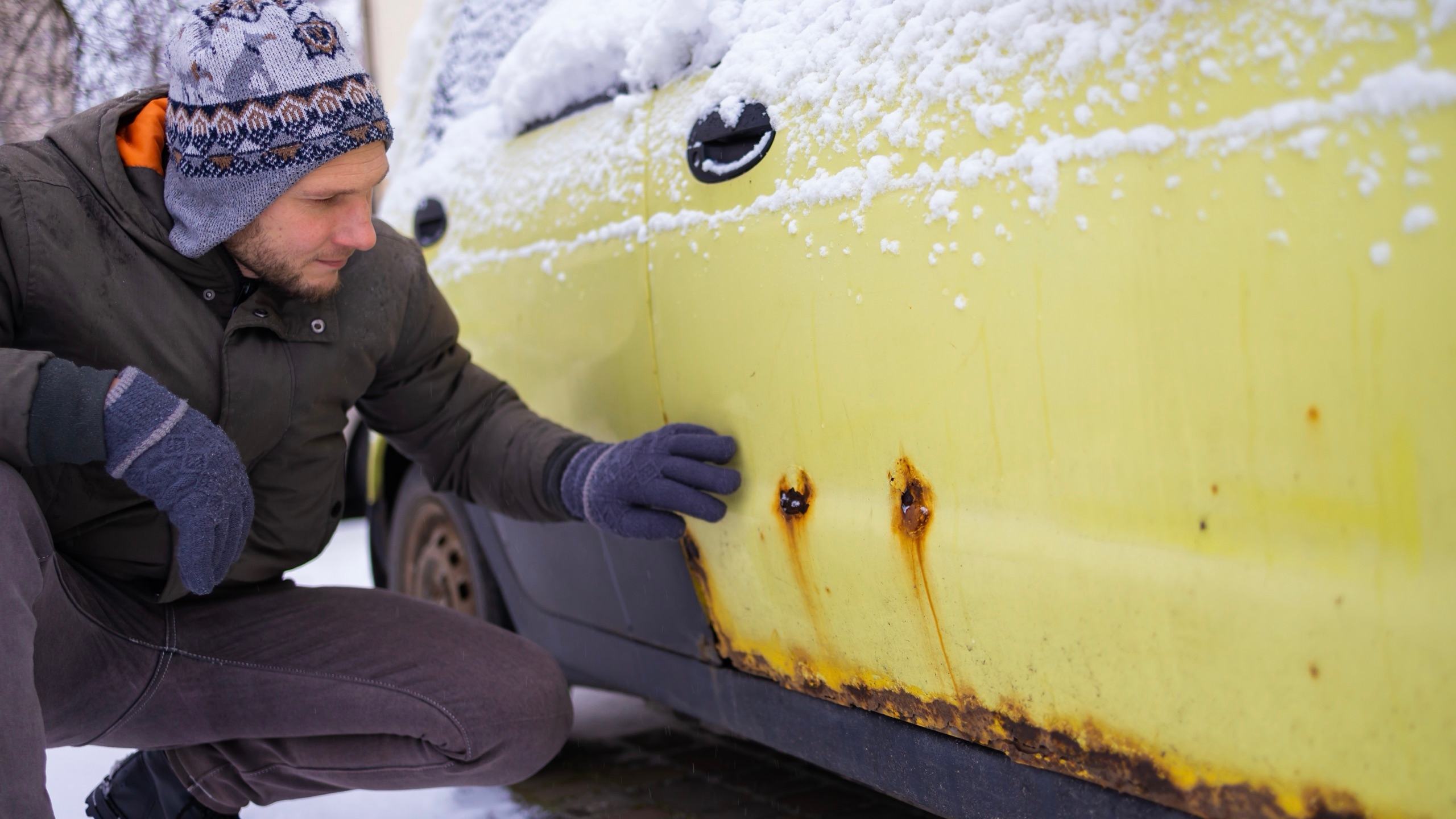 Un homme qui constate les dégâts de la rouille sur son auto.